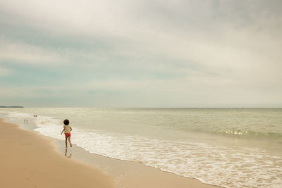 Rear view of woman walking at beach against sky