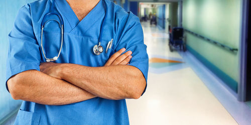 Midsection of man with arms raised standing against blue wall