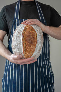 Close-up at bakers hands holding a loaf of organic sourdough bread in front of him.