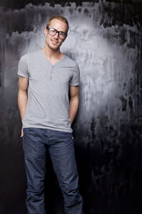 Portrait of young man wearing eyeglasses standing against old wall