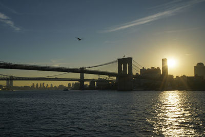 Silhouette bridge over river against sky during sunset