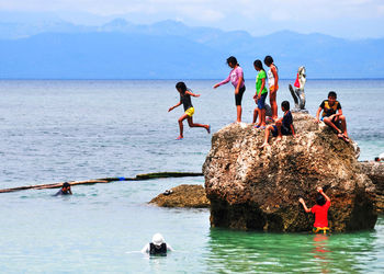 Children playing on rock formation in sea against sky