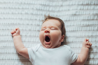 Directly above shot of cute baby yawning while lying on bed