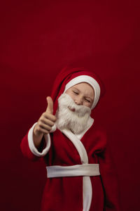 A boy in a santa claus costume holds his thumbs up.