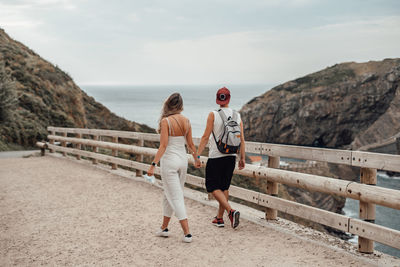 Rear view of couple walking on sea against sky