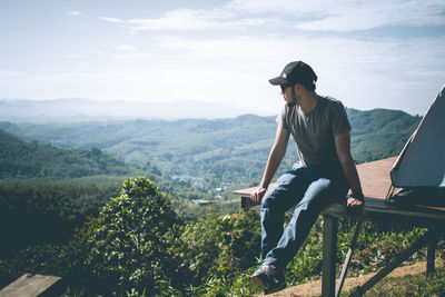 Full length of man sitting on mountain against sky