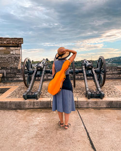 Rear view of woman with guitar case standing against sky