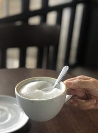 Close-up of hand holding a cup cappuccino coffee  on wood table blurred background