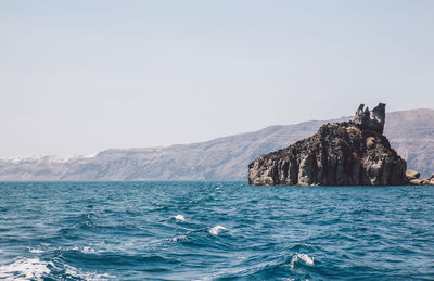 Scenic view of blue sea and rocky mountains against clear sky on sunny day