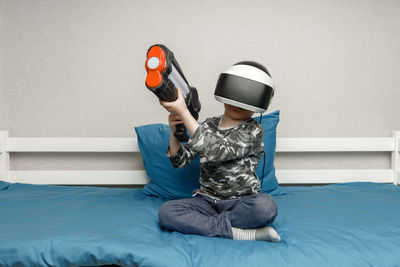 Full length of a boy holding camera while sitting against wall