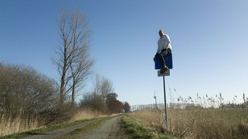 Man standing on road amidst field against clear sky