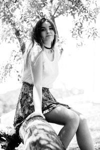 Smiling young woman sitting on tree trunk at park