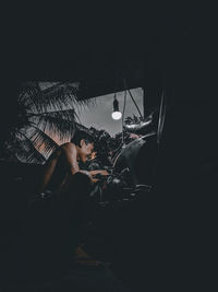 Side view of young woman sitting in the dark