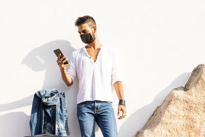 Young man using mobile phone standing against wall