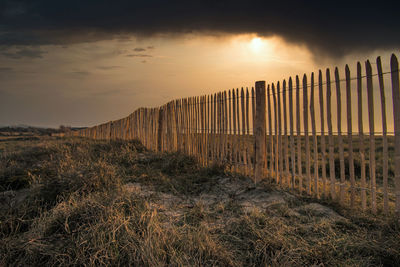 Wooden fence on field against sky during sunset