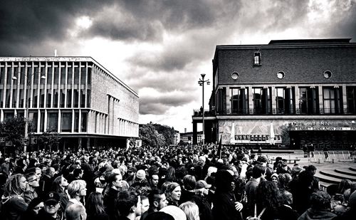 Group of people in front of buildings against cloudy sky