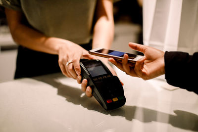 Cropped hand of young customer paying through mobile phone at fashion store