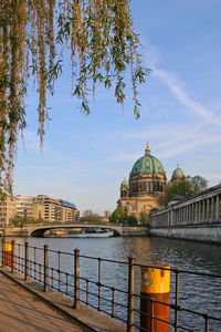 View of buildings by river in city against sky