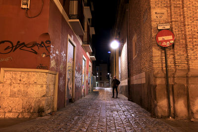 Rear view of woman walking on footpath amidst buildings