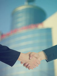 Cropped image of businesswomen shaking hands against building