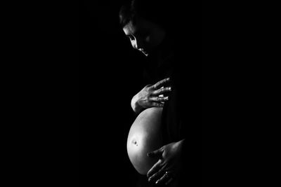 Pregnant woman standing against black background