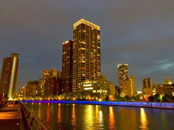 Illuminated buildings by river against sky at night