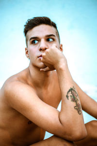 Portrait of shirtless young man against sky