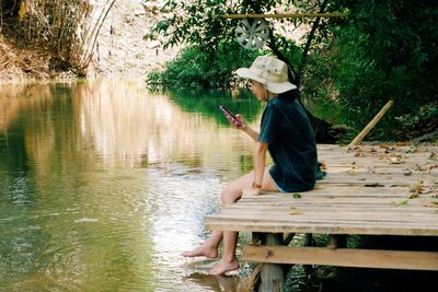 Side view of woman sitting on wood by lake