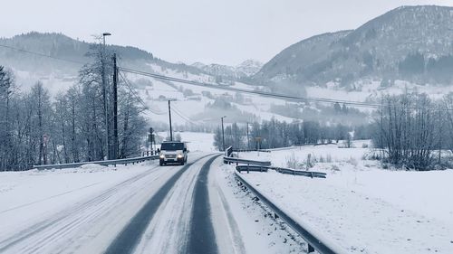 Snow covered road by mountain against sky during winter