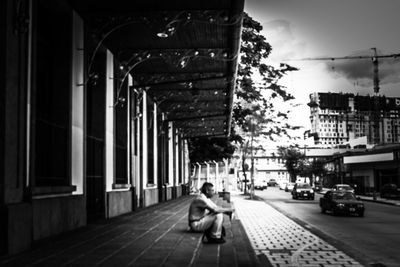 Rear view of woman sitting on street amidst buildings at night