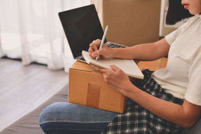 Midsection of woman writing in book while sitting at home