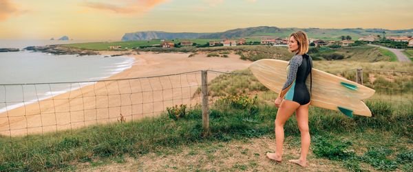 Surfer woman with wetsuit and surfboard looking at the beach