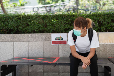 Young woman wearing mask looking away while sitting outdoors