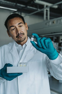 Scientist holding vaccine bottle and test tube tray while standing at laboratory