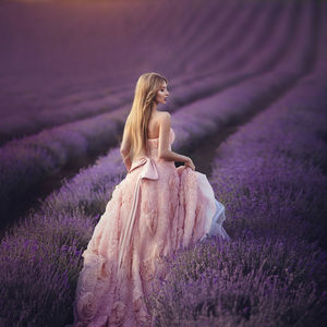 Rear view of woman standing by purple flower on field