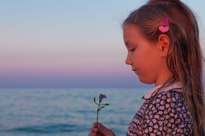 Adorable little girl looks on flower on beach.cute child with wet long hair in dress smelling flower