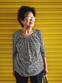Mature woman standing against yellow wall