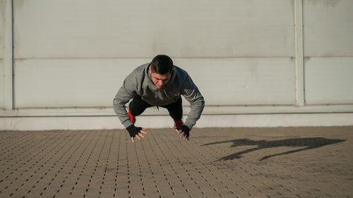 A man in a hoodie jumps while doing push-ups outdoors