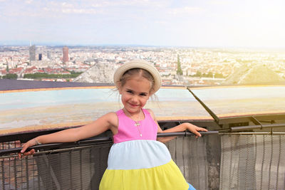Portrait of smiling girl standing on railing against cityscape