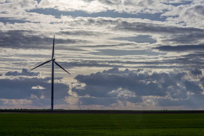 Windmill on land against cloudy sky during sunset