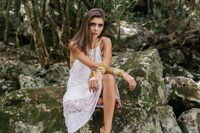 Portrait of young woman sitting on rock in forest