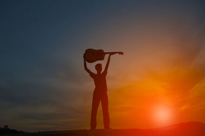 The shadow of a man holding a guitar on a hill with orange light