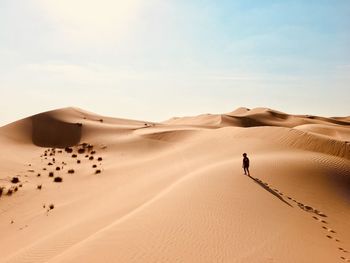 Rear view of boy walking in sand dune during sunny day