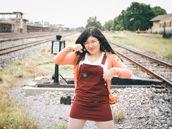 Portrait of smiling young woman standing on railroad track