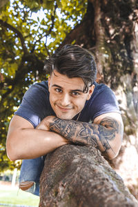 Portrait of young man lying on tree