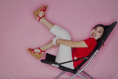 Side view of cheerful woman sitting on chair against pink background