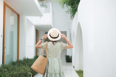 Woman holding hat standing against wall