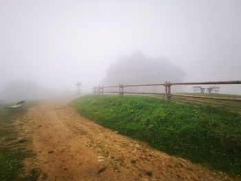 Road amidst field against sky during foggy weather