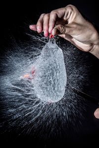 Close-up of human hand holding bursting water balloon against black background