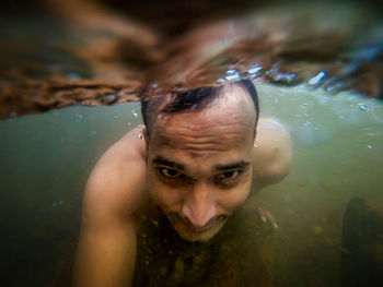 Man swimming in natural waterfall underwater shot from low angle